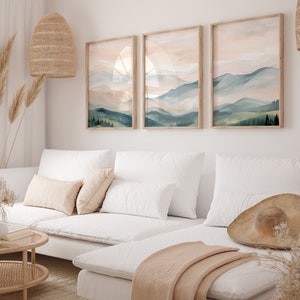 May include: A white sectional sofa with a light brown throw blanket and a large brown hat on the seat. Three framed watercolor paintings of mountains and trees hang on the wall behind the sofa.