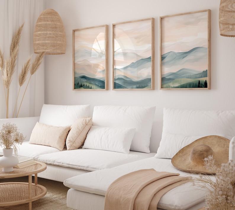 May include: A white sectional sofa with a light brown throw blanket and a large brown hat on the seat. Three framed watercolor paintings of mountains and trees hang on the wall behind the sofa.