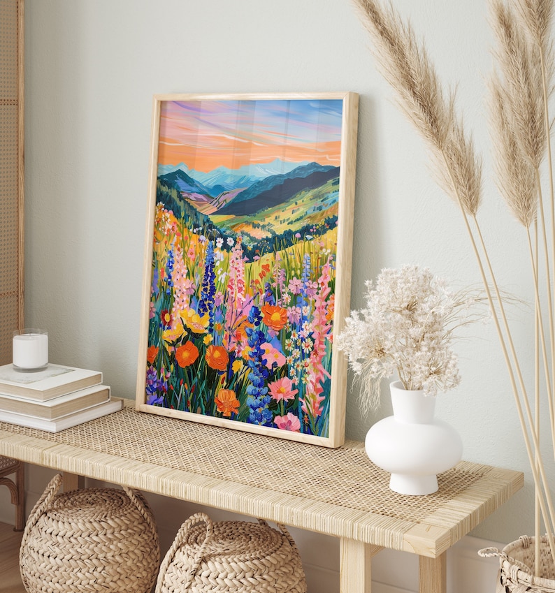 May include: A framed print of a colorful landscape painting featuring a field of wildflowers in the foreground and a mountain range in the background. The painting is in a wooden frame and is hanging on a wall.