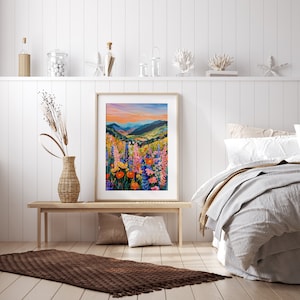 May include: A framed print of a colorful landscape painting featuring a field of wildflowers in the foreground and a mountain range in the background. The sky is a vibrant orange and pink.