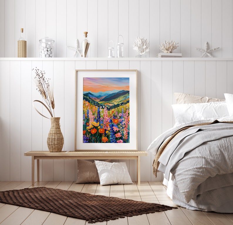 May include: A framed print of a colorful landscape painting featuring a field of wildflowers in the foreground and a mountain range in the background. The sky is a vibrant orange and pink.