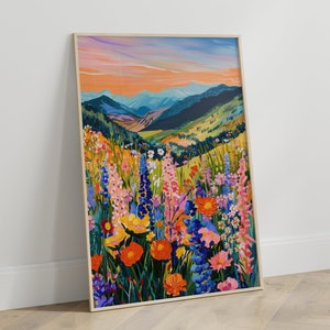 May include: A framed painting of a mountain landscape with a field of colorful wildflowers in the foreground. The sky is a vibrant orange and pink, and the mountains are a deep blue. The wildflowers are a variety of colors, including pink, purple, yellow, and orange.