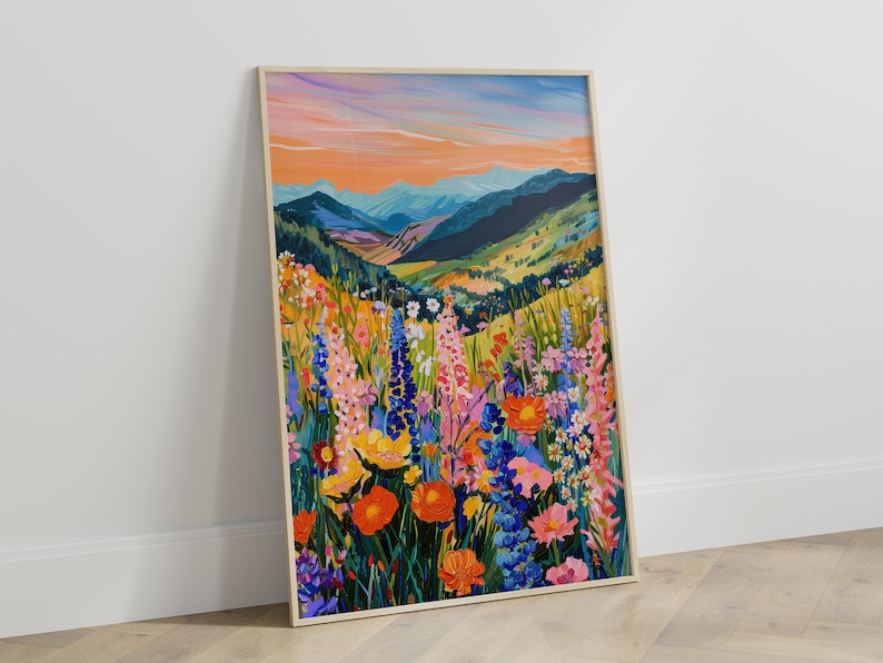 May include: A framed painting of a mountain landscape with a field of colorful wildflowers in the foreground. The sky is a vibrant orange and pink, and the mountains are a deep blue. The wildflowers are a variety of colors, including pink, purple, yellow, and orange.