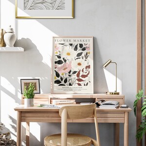 May include: A light wood desk with a gold lamp, a potted plant, and a framed print of flowers with the text "FLOWER MARKET BOTANICAL COLLECTION".