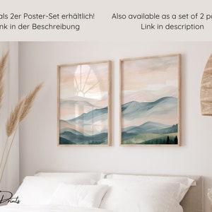 May include: Two framed watercolor landscape prints with a mountain range and a sunrise in the background. The prints are hanging on a white wall above a bed with white bedding. The text "Also available as a set of 2 posters! Link in description" is at the top of the image.
