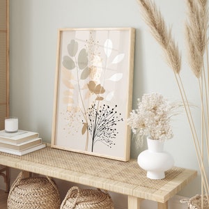 May include: A framed print with a beige background and a stylized floral design in shades of brown, black, and white. The print is hanging on a light green wall above a wooden bench with a woven rattan top.