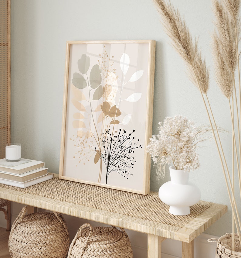 May include: A framed print with a beige background and a stylized floral design in shades of brown, black, and white. The print is hanging on a light green wall above a wooden bench with a woven rattan top.