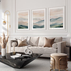 May include: A white sofa with three pillows, a black coffee table with a magazine on it, and a gold and beige ottoman. The sofa is in front of a white wall with three framed landscape paintings.