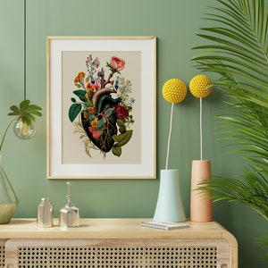 May include: A framed botanical print of a human heart with flowers growing from it. The print is on a light beige background with a wooden frame. The print is hanging on a green wall with a vase of flowers and a plant in the background.