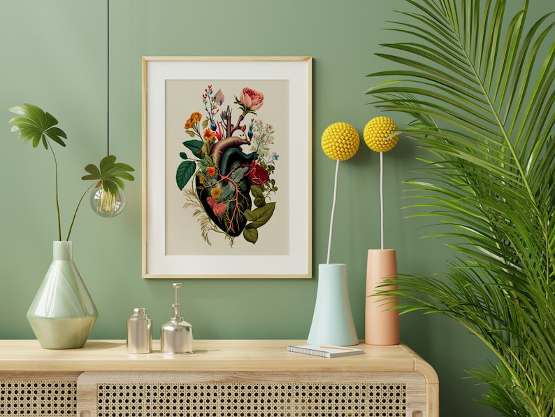 May include: A framed botanical print of a human heart with flowers growing from it. The print is on a light beige background with a wooden frame. The print is hanging on a green wall with a vase of flowers and a plant in the background.