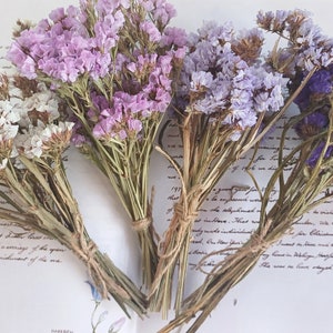 May include: Four bunches of dried flowers in shades of white, light purple, lavender, and purple. The flowers are tied together with twine.