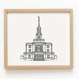 May include: A framed black and white line drawing of a building with a tall spire. The architectural illustration features a symmetrical design with multiple windows and a detailed facade. The artwork is set against a white background within a light-colored wooden frame.