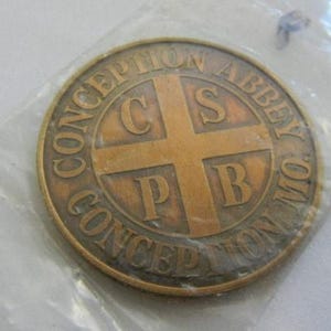 May include: A gold-colored metal token with the words "Conception Abbey" and "Conception" around the edge. In the center is a cross with the letters "C.S.P.B."