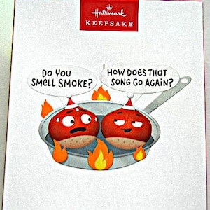 May include: A Hallmark Keepsake box featuring an illustration of two cartoon chestnuts wearing Santa hats inside a silver frying pan over orange flames. Speech bubbles contain the text: Do You SMELL SMOKE? and HOW DOES THAT SONG GO AGAIN?
