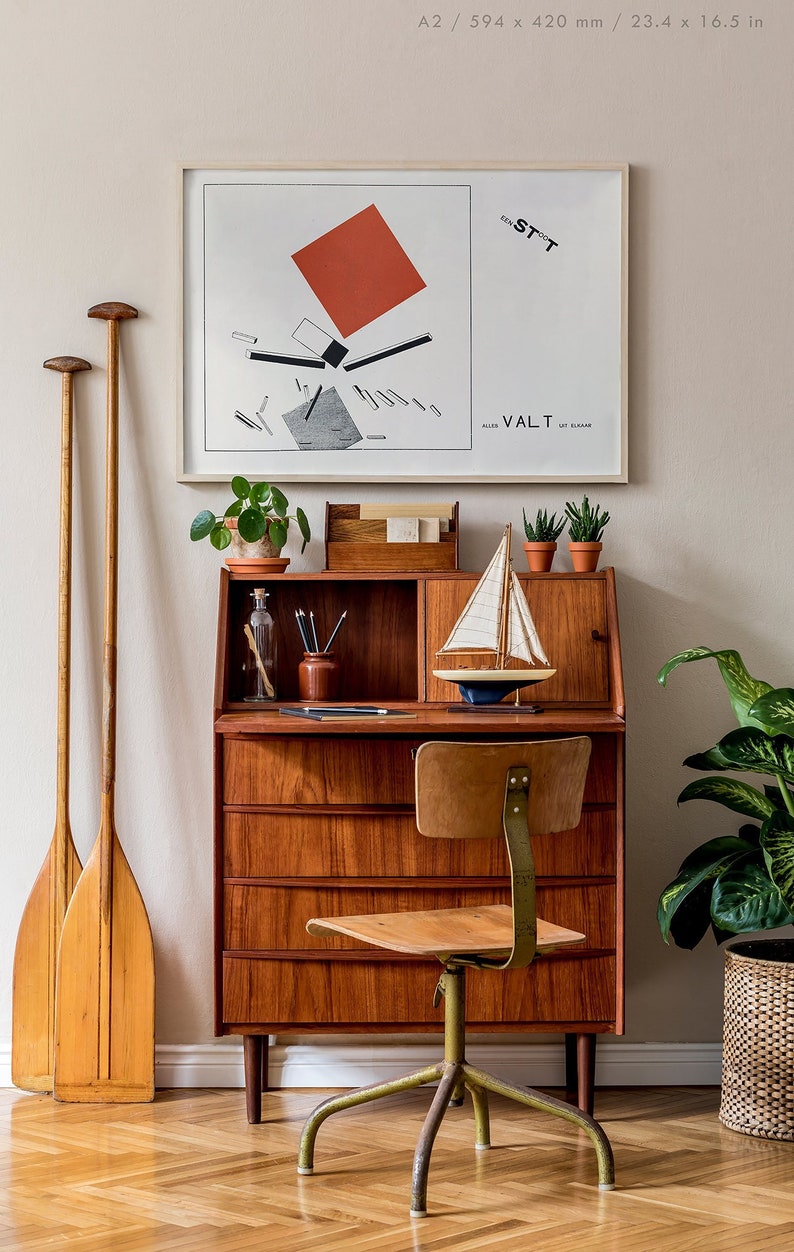 May include: A mid-century modern desk with a framed abstract art print, a small sailboat model, and potted plants. Two wooden oars lean against the wall. The desk is made of wood and has a matching chair.