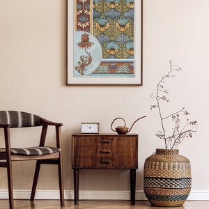 May include: A framed print of a vintage floral design with blue, green, yellow, and brown colours. The print is hanging on a white wall above a wooden dresser with three drawers. A brown wicker vase with a dried plant is on the right side of the dresser.