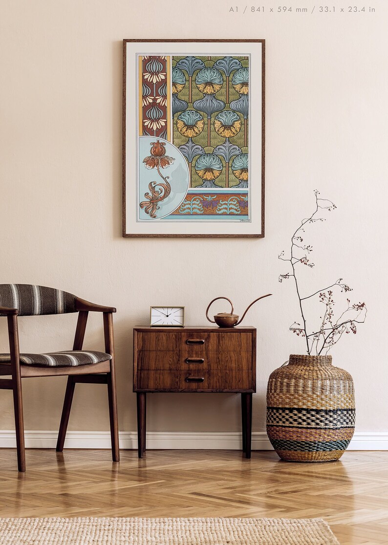 May include: A framed print of a vintage floral design with blue, green, yellow, and brown colours. The print is hanging on a white wall above a wooden dresser with three drawers. A brown wicker vase with a dried plant is on the right side of the dresser.