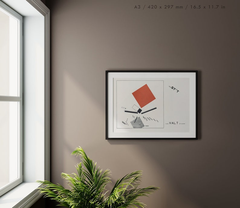 May include: A framed art print featuring a geometric abstract design with a red square, black lines, and gray shapes on a white background. The print is in a black frame and is displayed on a brown wall near a window and a green plant.