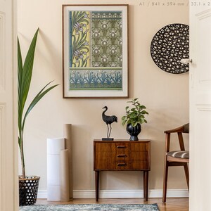 May include: A framed print of a vintage floral design in shades of green, yellow, and white. The print is hanging on a light beige wall above a wooden side table with a black crane sculpture and a potted plant.