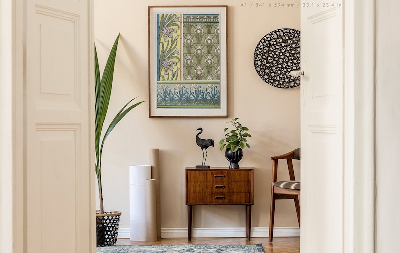 May include: A framed print of a vintage floral design in shades of green, yellow, and white. The print is hanging on a light beige wall above a wooden side table with a black crane sculpture and a potted plant.