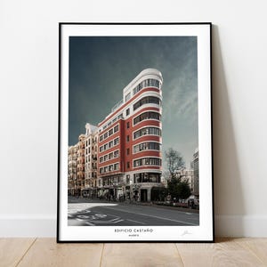 May include: A framed photograph of a red brick building with white trim in Madrid, Spain. The building is called "Edificio Castaño".