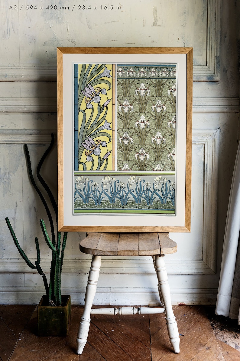 May include: A framed print of a vintage botanical illustration featuring a repeating pattern of stylized iris flowers in shades of green, yellow, blue, and white. The print is in a wooden frame and is sitting on a wooden stool.