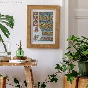 May include: A framed print featuring a floral design in shades of blue, yellow, and red. The print is hanging on a white wall, with plants in pots on a wooden table in the foreground.