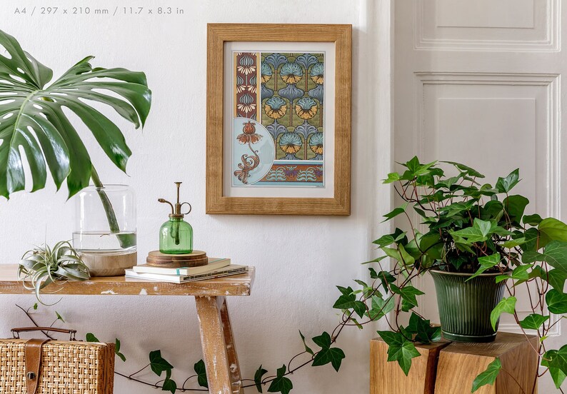 May include: A framed print featuring a floral design in shades of blue, yellow, and red. The print is hanging on a white wall, with plants in pots on a wooden table in the foreground.