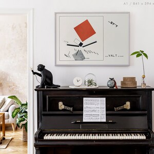 May include: A black upright piano with a framed abstract art print and decorative items. A black monkey statue holds a light. The art print features a red square and geometric shapes. A clock, glass dome, and small boxes sit on the piano.