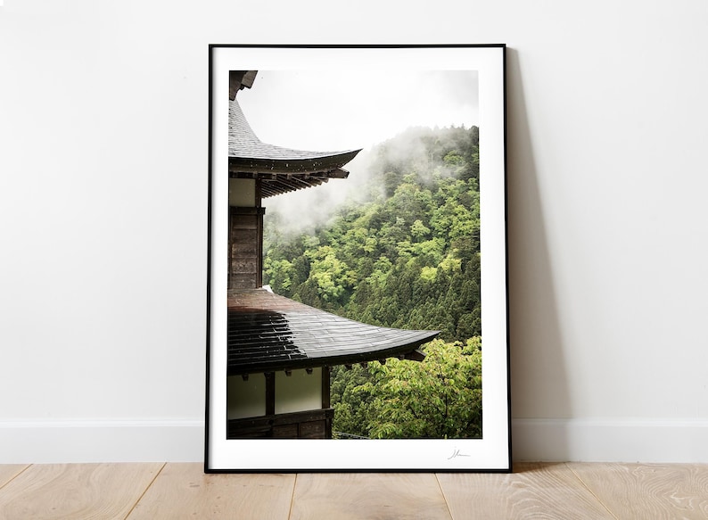 May include: A black and wooden Japanese temple roof with a view of a lush green forest with fog in the background.