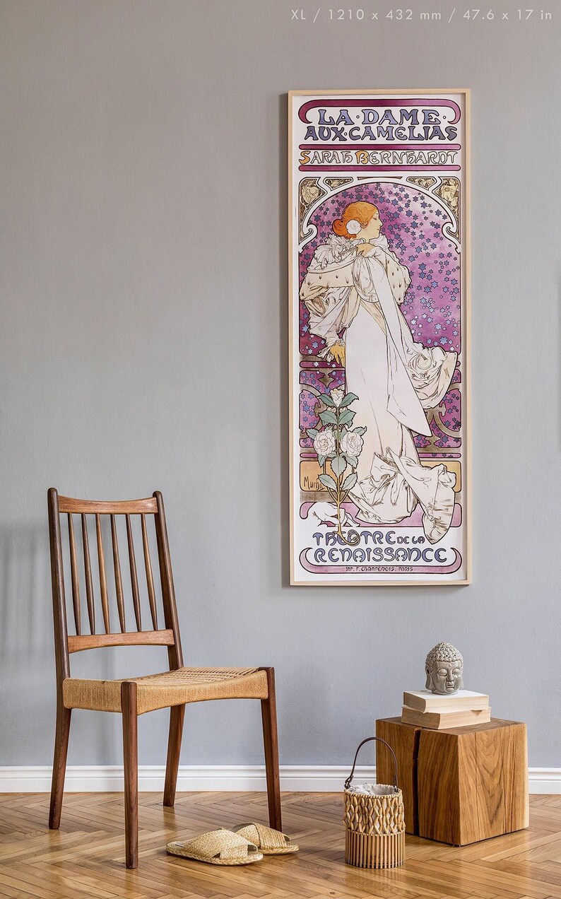 May include: A vintage poster featuring a woman in a white dress with a floral design. The poster is framed in wood and has the text "LA DAME AUX CAMELIAS SARAH BERNHARDT THEATRE DE LA RENAISSANCE" printed on it.
