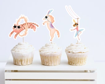 May include: Three cupcakes with circus-themed toppers. The first cupcake has a tiger wearing sunglasses jumping through a ring of fire. The second cupcake has a pink horse wearing sunglasses and a colourful saddle. The third cupcake has a girl wearing a pink dress and sunglasses hanging from a trapeze.