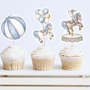 May include: Three cupcake toppers featuring a blue and white striped beach ball, a white horse on a carousel, and a white horse with blue balloons. The toppers are on top of cupcakes with white frosting.
