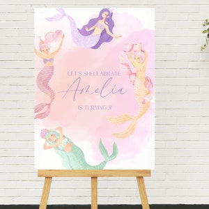 May include: A pink and purple mermaid-themed birthday party sign with the text "Let's Shell-abrate Amelia is turning 3!" and four mermaids with colorful tails.