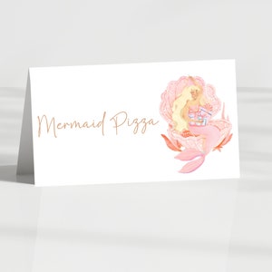May include: A pink and white place card with the text "Mermaid Pizza" in brown script. A mermaid with blonde hair sits inside a pink seashell with a blue and white gift.