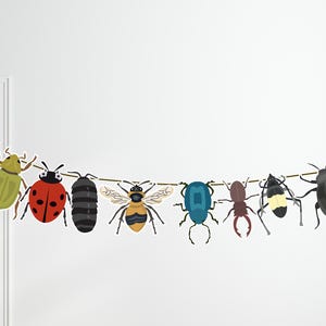 May include: A string of colorful bug cutouts, including a ladybug, a bee, a green beetle, and a blue beetle, hangs on a white wall.