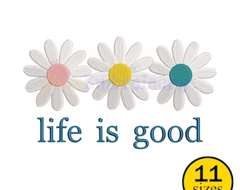 Może przedstawiać: Trzy białe kwiaty stokrotki z różowymi, żółtymi i turkusowymi środkami, nad frazą "life is good" w kolorze niebieskim. Żółte koło z napisem "11 rozmiarów" znajduje się w prawym dolnym rogu. Obraz jest na białym tle.