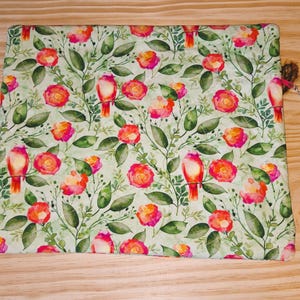 K&ouml;nnte beinhalten: Rechteckiger Stoff mit floralem Muster auf hellgr&uuml;nem Hintergrund. Das Muster zeigt rote und rosa Rosen, gr&uuml;ne Bl&auml;tter und rote V&ouml;gel. Eine braune Quaste mit einem silbernen Anh&auml;nger ist an der Seite befestigt.