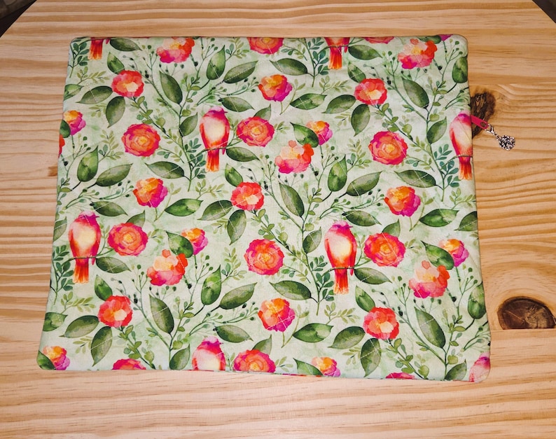 K&ouml;nnte beinhalten: Rechteckiger Stoff mit floralem Muster auf hellgr&uuml;nem Hintergrund. Das Muster zeigt rote und rosa Rosen, gr&uuml;ne Bl&auml;tter und rote V&ouml;gel. Eine braune Quaste mit einem silbernen Anh&auml;nger ist an der Seite befestigt.