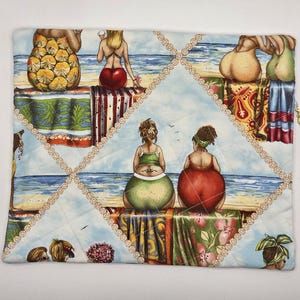 May include: A rectangular quilted fabric pouch featuring a repeating beach scene print. The design depicts multiple figures sitting on towels by the ocean, rendered in vibrant colors including red, green, and yellow. A gold-toned zipper pull is visible.