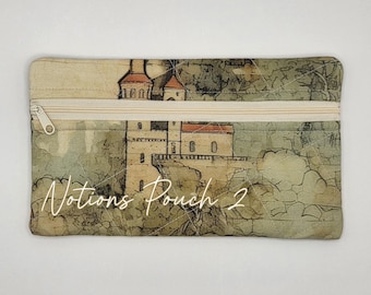 May include: A rectangular fabric pouch featuring a beige zipper closure and a printed design of a castle on a cliffside. The fabric has a quilted diamond pattern and the white text "Notions Pouch 2" is printed across the lower section of the pouch.