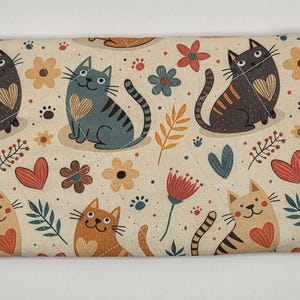 May include: A rectangular fabric pouch featuring a cream background with a repeating pattern of cats in various colors, including black, gray, orange, and tan. Each cat has a heart on its chest. The design includes small flowers, leaves, and hearts.