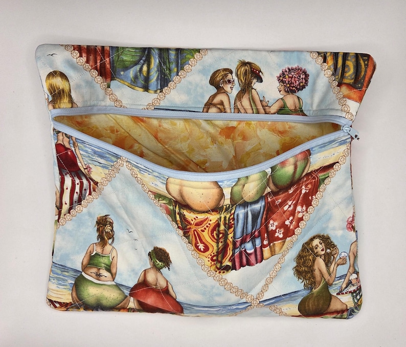 May include: A rectangular fabric pouch with a light blue zipper closure. The exterior features a repeating print of illustrated figures relaxing on a beach, accented by a decorative beige chain-link pattern. The interior lining is a warm orange.