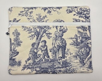 May include: A rectangular zippered pouch made of cream-colored fabric featuring a blue toile print of figures in a landscape. The pouch has a white zipper closure with a small decorative charm attached to the pull, and visible quilted stitching.