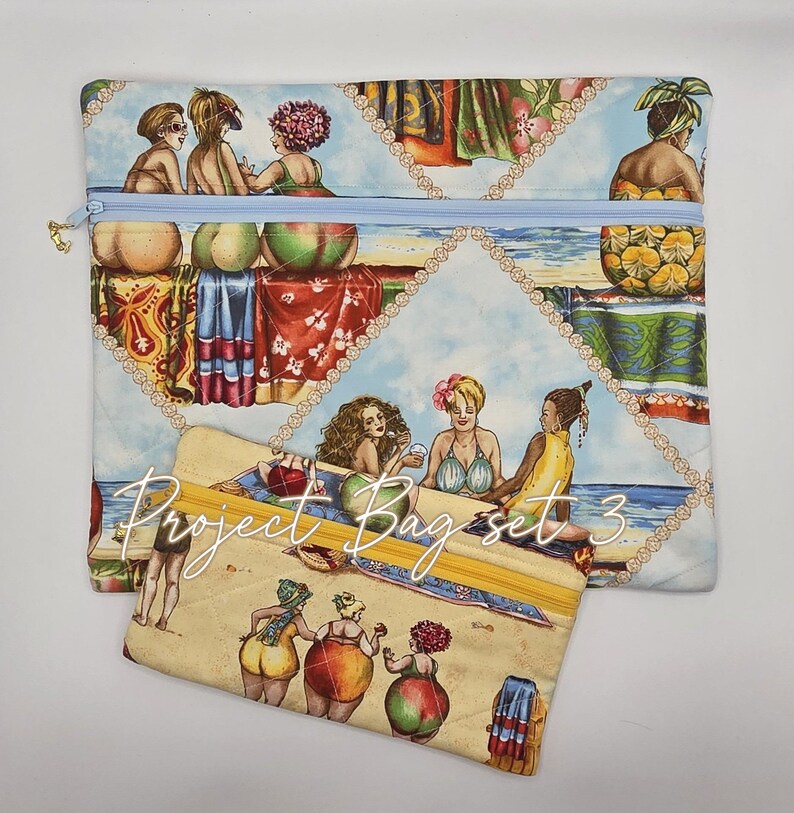 May include: Two rectangular fabric pouches featuring a repeating print of people at the beach. The larger pouch has a light blue zipper, while the smaller pouch has a yellow zipper and the text Project Bag set 3 printed across the front surface.