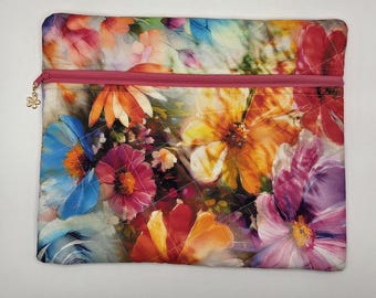 May include: A rectangular quilted pouch featuring a vibrant, multi-colored floral print with shades of blue, orange, pink, and yellow. The pouch includes a pink zipper closure along the top edge, accented by a small, gold-toned flower-shaped charm.