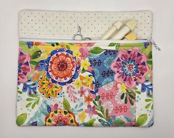 May include: A rectangular fabric pouch featuring a vibrant floral pattern with pink, orange, yellow, and blue flowers on a white background. The top section is cream-colored with small dots and a white zipper closure containing metal scissors and tools.
