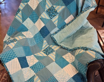 May include: A patchwork quilt featuring a star pattern composed of various fabric squares in shades of teal, light blue, white, and yellow. The quilt displays a mix of geometric, striped, and floral prints, with a solid light blue fabric backing.