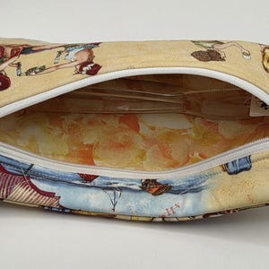 May include: A rectangular fabric zipper pouch featuring a beige exterior with a repeating illustration of figures in red and blue clothing. The interior is lined with a light orange and yellow patterned fabric, and a white zipper runs across the top.