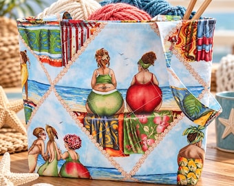 May include: A fabric tote bag featuring a beach scene with multiple figures in swimwear, separated by a diamond-patterned border. The bag is filled with balls of yarn and two wooden knitting needles. The print includes blue, green, red, and yellow colors.